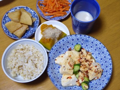 青い皿に持った豆腐や茶碗に玄米、小皿にかぼちゃや人参の副菜など