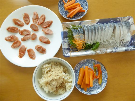 テーブルに並んだしめ鯖や切った魚肉ソーセージ、茶碗には玄米